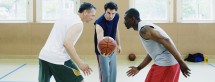 Two young men and a mid adult man playing basketball in the basketball court