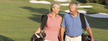 Senior Couple Walking Along Golf Course Carrying Bags